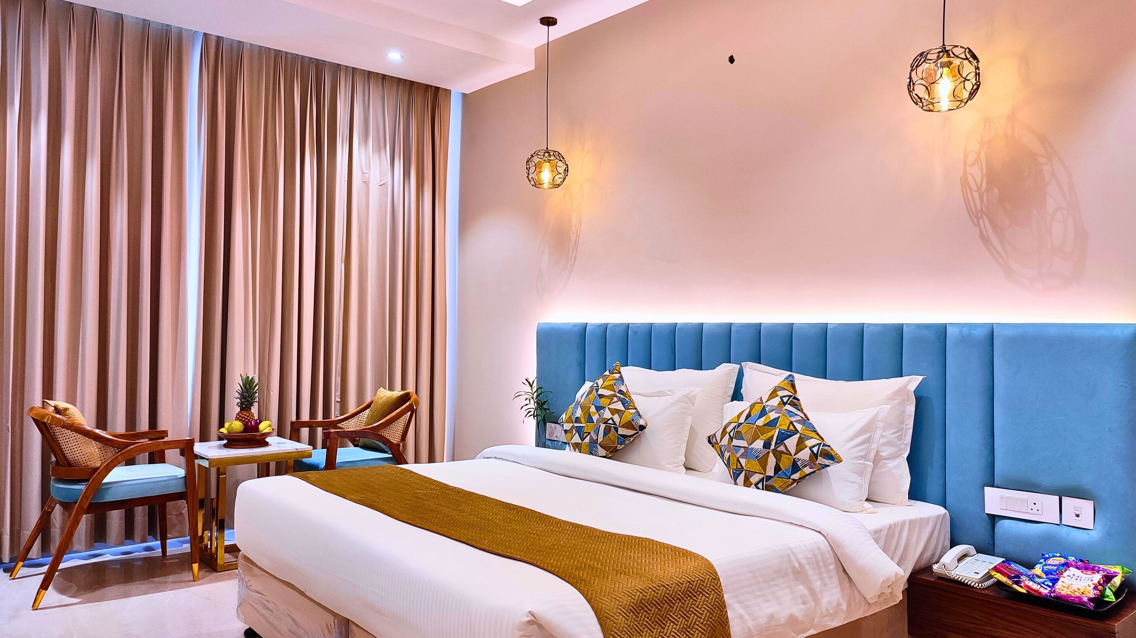 Habitación de hotel con una cama grande, dos sillas, una mesita con fruta y un teléfono junto a la cama.