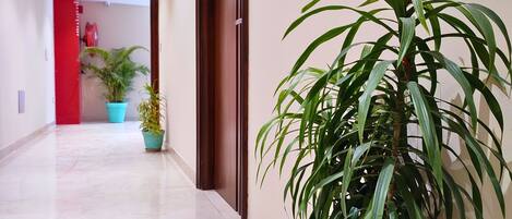 A hallway with a marble floor, potted plants, and a red door.