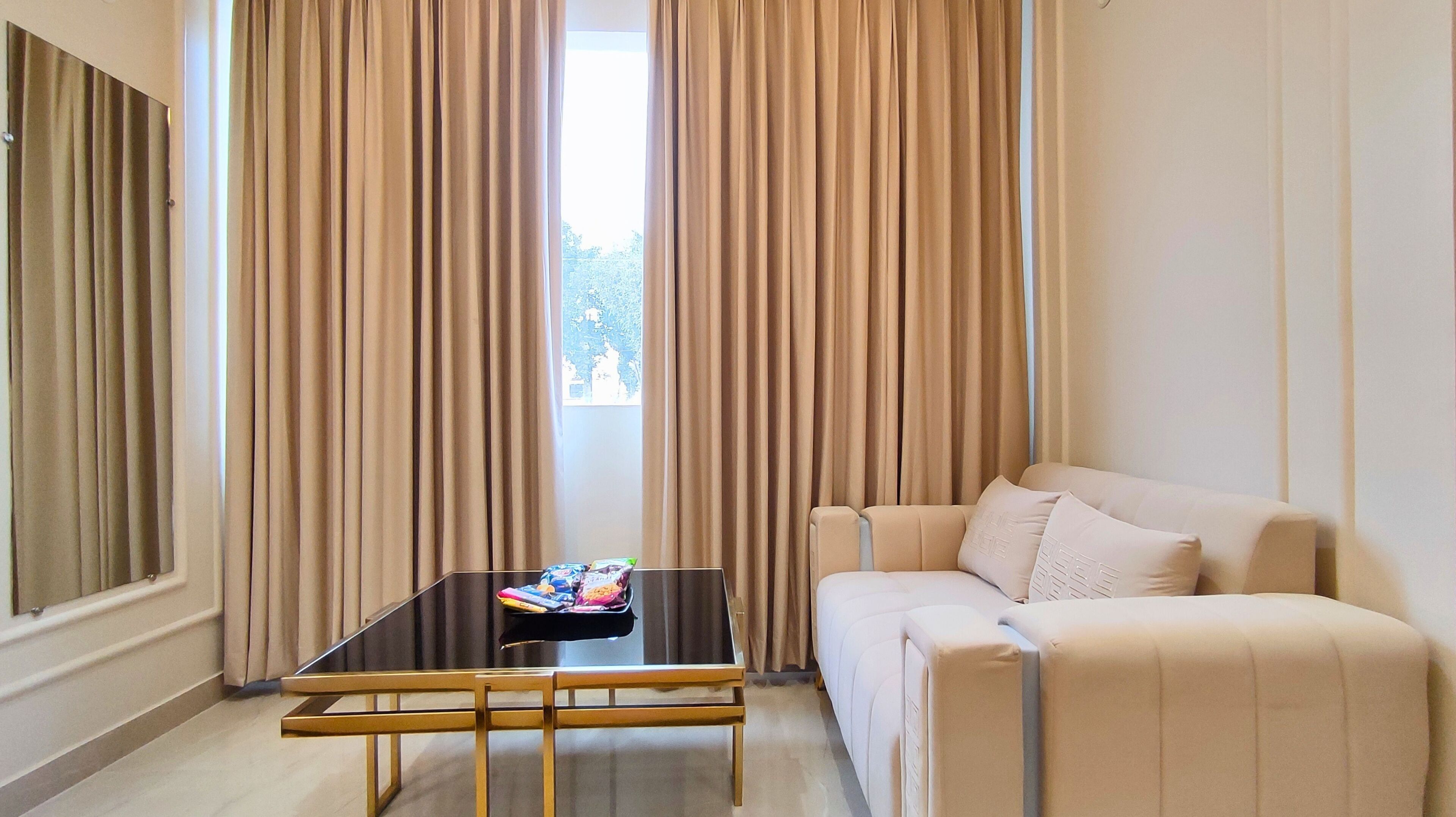 A room with a beige sofa, a glass coffee table, and beige curtains.