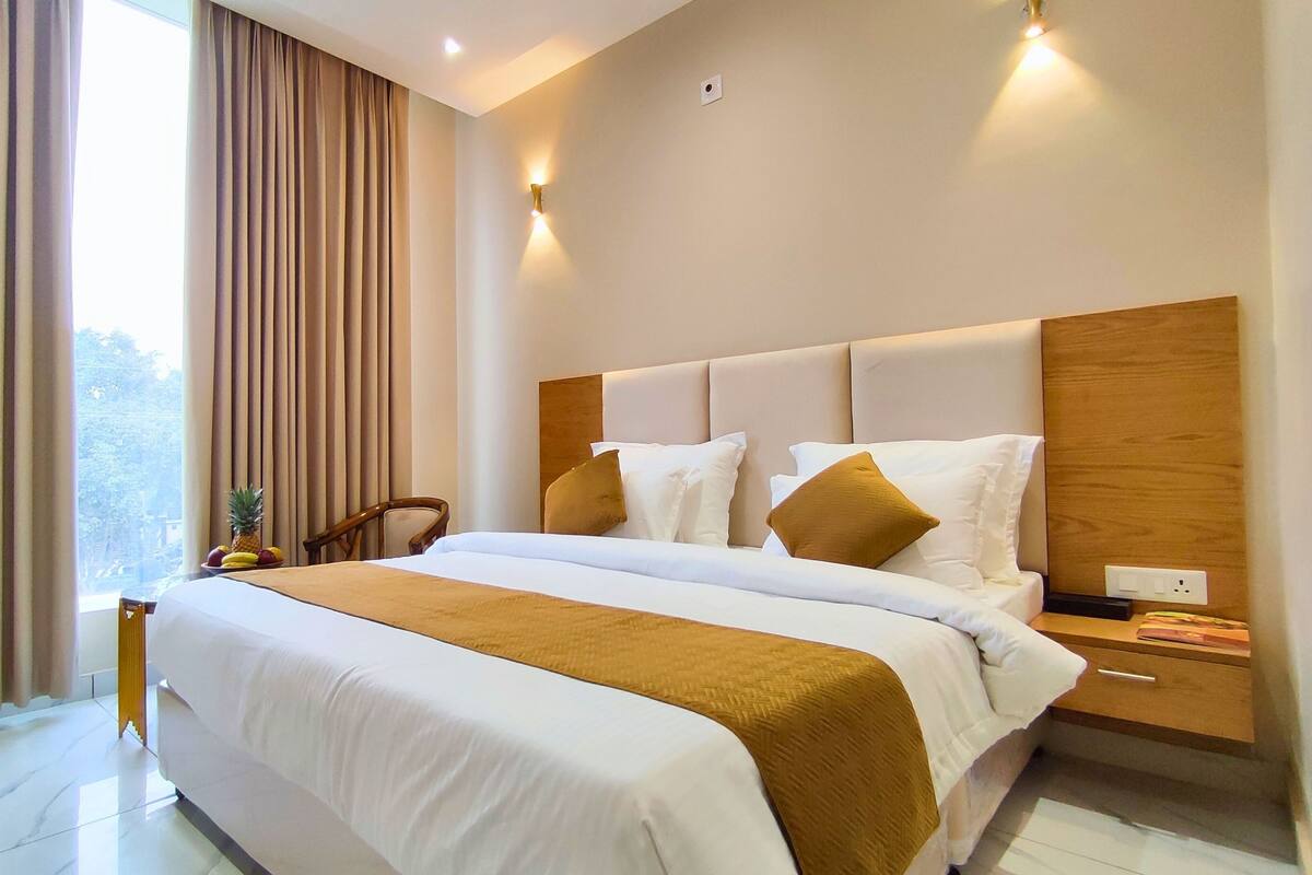 Une chambre d’hôtel moderne avec un grand lit, une tête de lit en bois et une table de chevet avec une lampe.