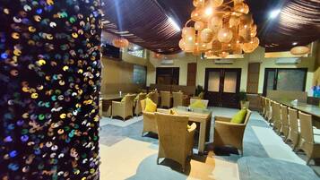 A restaurant with wicker furniture, glass tables, and hanging lights.