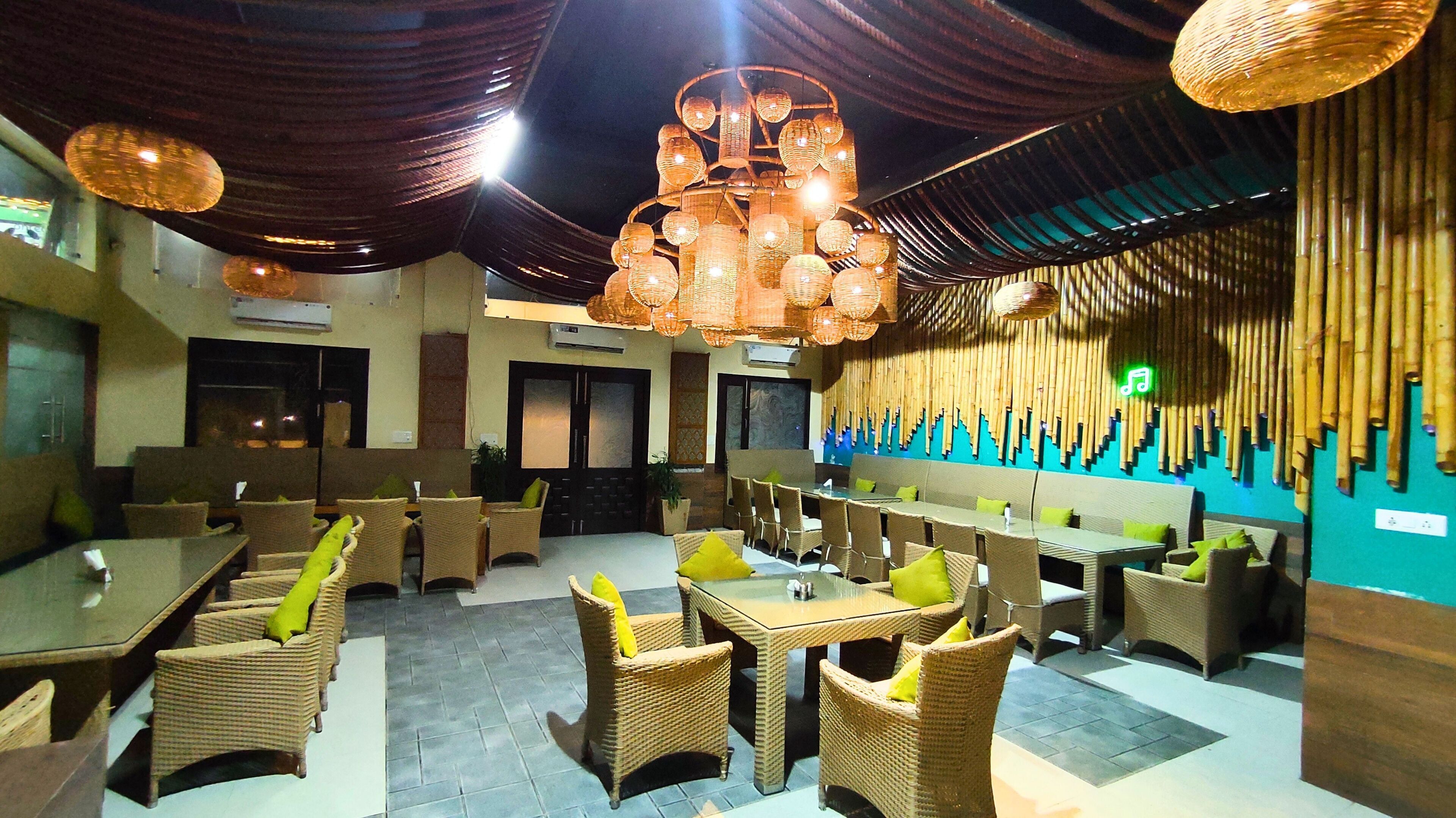 Un restaurante con mobiliario de mimbre, luces colgantes y un muro de bambú.