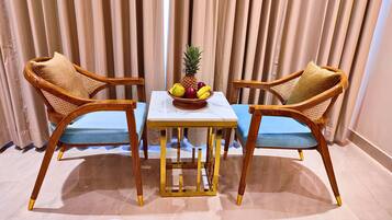 A dining area with two wooden chairs and a table, a fruit bowl on the table, and a curtain backdrop.