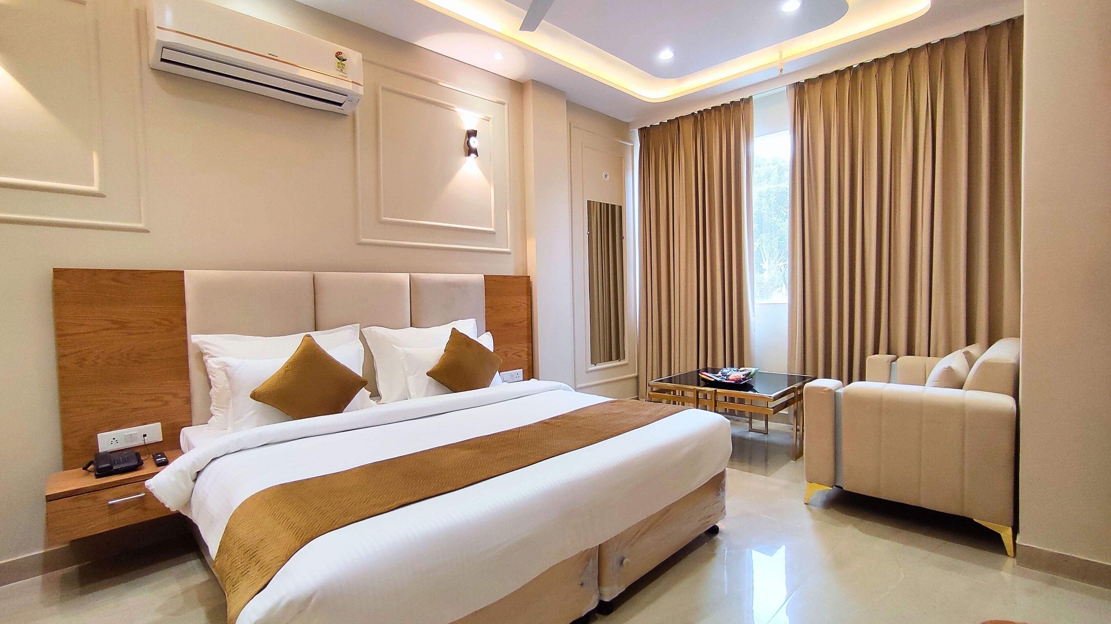 A hotel room with a large bed, a sofa, a small table, and a window with curtains.