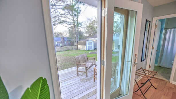 A room with a sliding glass door leading to a wooden deck, a small seating area, and a drying rack. - Central Island Home (Charleston)