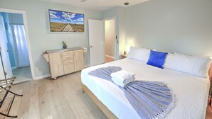A bedroom with a bed, a ceiling fan, a wooden dresser, a painting, and a view of a corridor. - Central Island Home (Charleston)