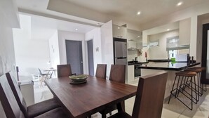 Une cuisine moderne dotée d’un îlot central, d’un coin repas avec une table et des chaises en bois, et d’une porte visible donnant sur une autre pièce.