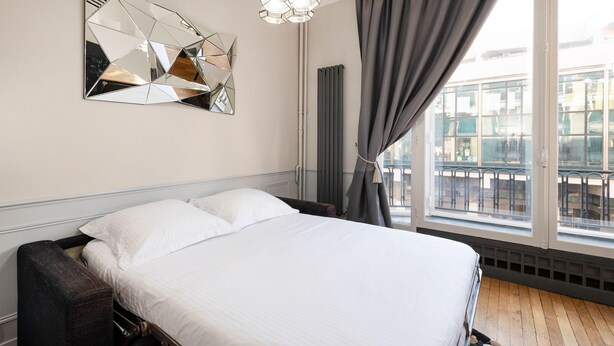 A hotel room with a bed, a large window with curtains, a geometric mirror on the wall, and a hanging light fixture. - MARSI LOVELY HOTEL DE VILLE C (Paris)