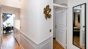 A hallway with white walls, a gold decorative element, and a door leading to a bedroom. - MARSI LOVELY HOTEL DE VILLE C (Paris)