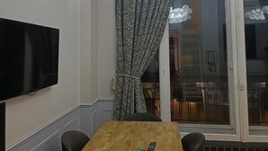 A dining area with a wooden table, black chairs, a television mounted on the wall, and a ceiling light fixture. - MARSI LOVELY HOTEL DE VILLE C (Paris)