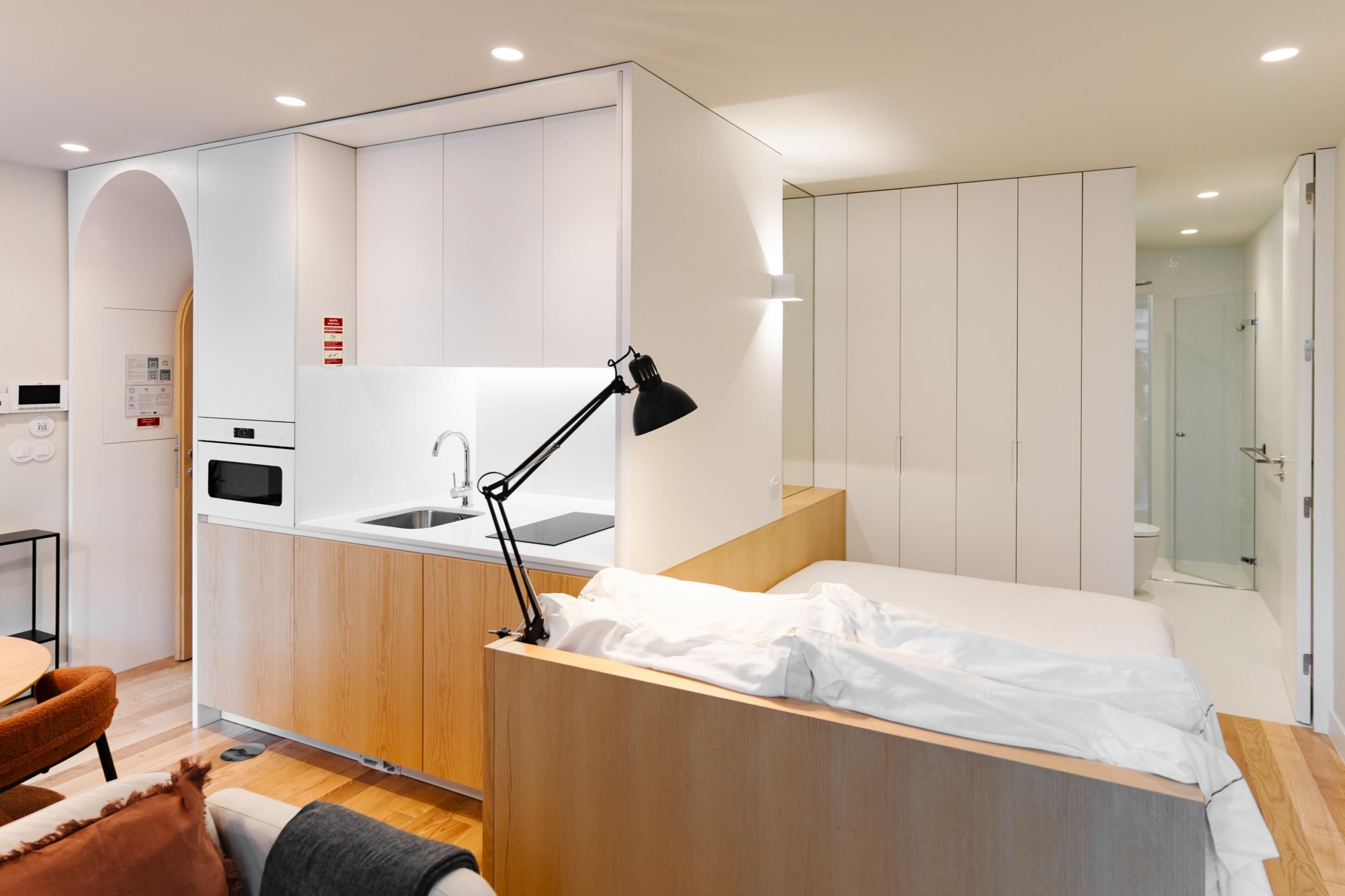 A compact hotel room with a kitchenette, a bed, a desk, and a bathroom.