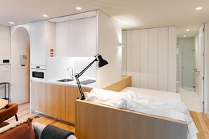 Habitación de hotel compacta con kitchenette, cama, escritorio y baño.