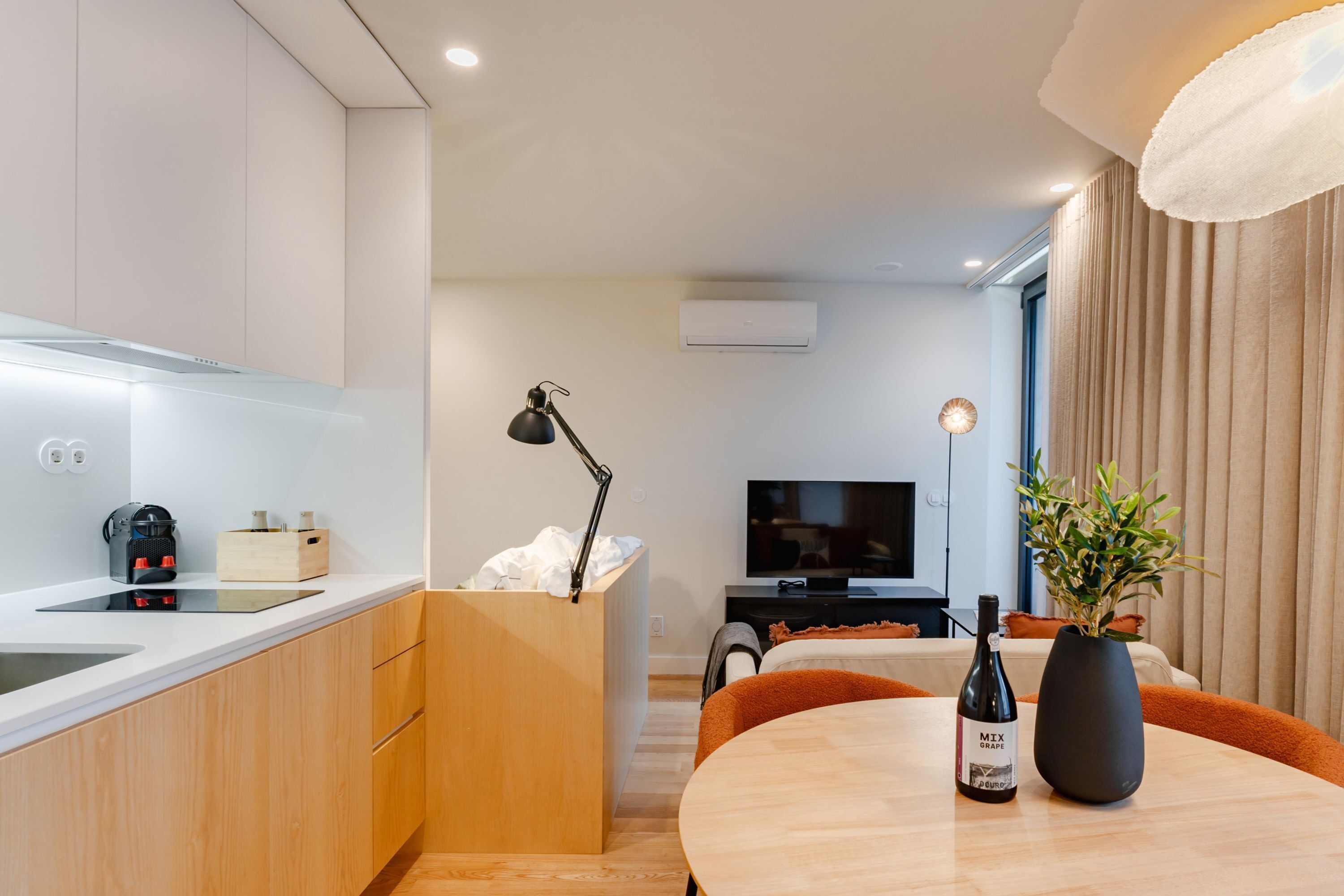 A modern kitchen with a built-in oven, a dining area with a table and chairs, a television, and a potted plant.