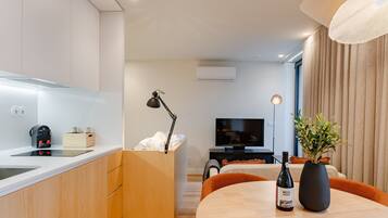 A modern kitchen with a built-in oven, a dining area with a table and chairs, a television, and a potted plant.