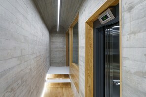 Um corredor estreito com piso de madeira, parede de concreto e uma porta com visor digital.