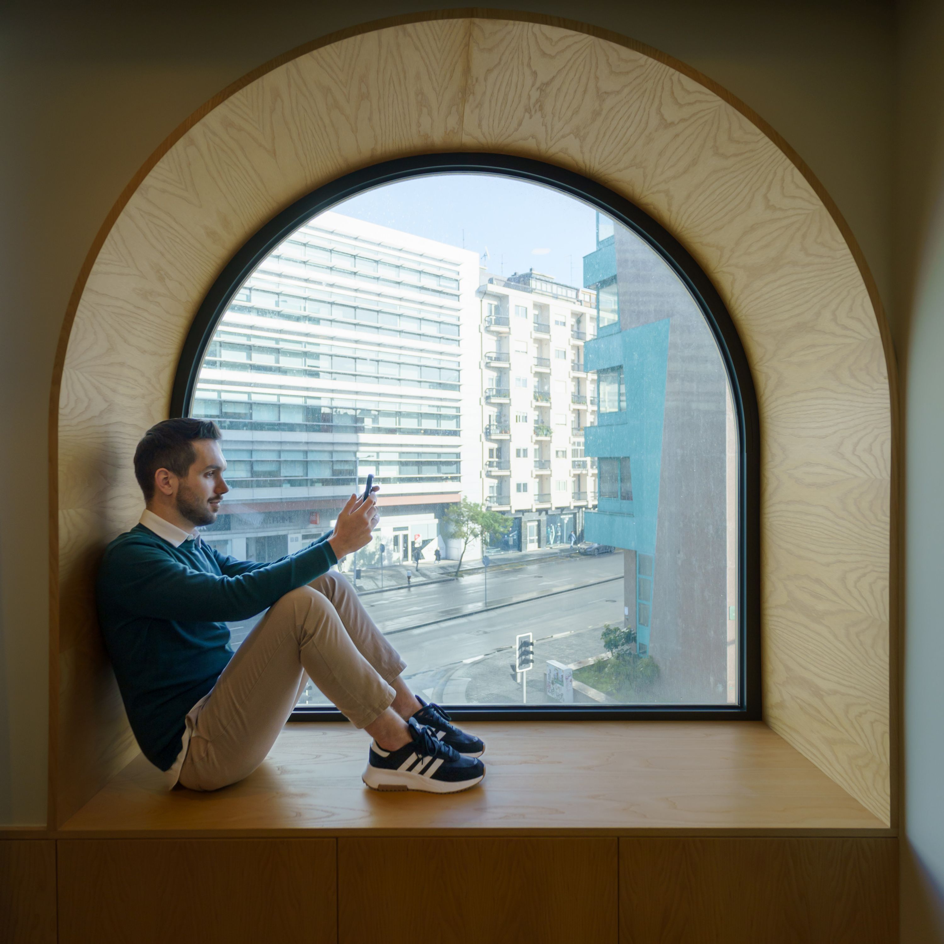 A person sitting by a large arched window with a view of a cityscape.