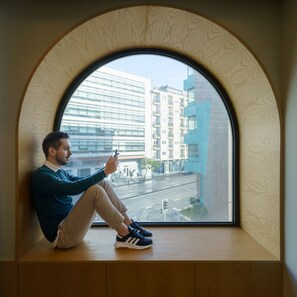A person sitting by a large arched window with a view of a cityscape. - Feel Porto Corporate Housing Boavista VI (Porto)