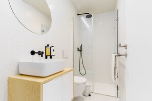 A modern bathroom with a white sink, a mirror, a toilet, and a glass-enclosed shower. - Feel Porto Corporate Housing Boavista VI (Porto)