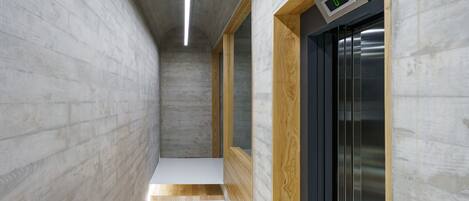 Un couloir étroit doté d’un plancher en bois, d’un mur en béton et d’une porte munie d’un écran numérique.