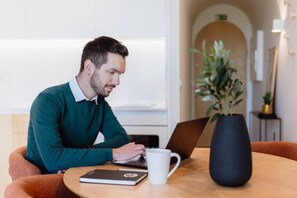 A person working on a laptop at a wooden table with a white mug and a notebook. - Feel Porto Corporate Housing Boavista II (Porto)