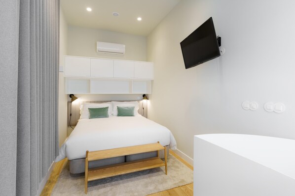 Un dormitorio moderno con cama, mesitas de noche, televisor montado y aire acondicionado integrado.