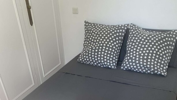 Ein ordentlich bezogenes Bett mit einem gefalteten Handtuch, zwei gestreiften Kissen und einer weißen Tür mit Messingbeschlag.