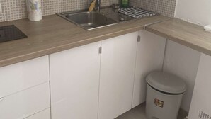 Eine Küche mit weißen Schränken, einer Edelstahl-Spüle, einer Fliesenküche und einem Mülleimer.