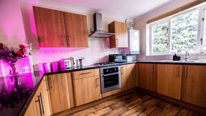 A modern kitchen with wooden cabinets, a stainless steel range hood, and a large window providing a view of a forested area. - Sleeps8-kingbeds-sofabed-garden-aircon-freeparking (London)