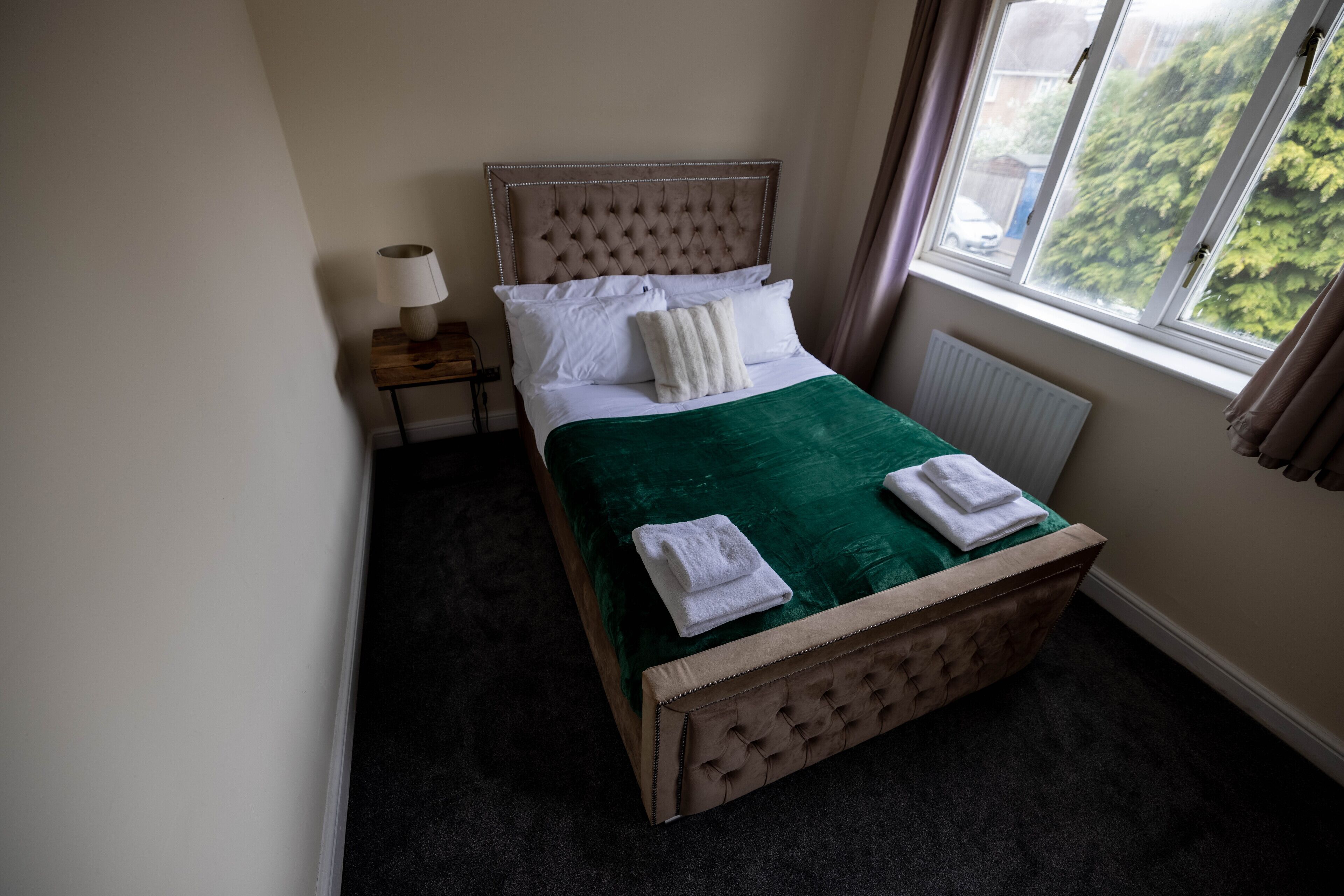 Ein ordentlich bezogenes Bett mit grüner Bettdecke, weißen Kissen und einem Holzkopfteil.