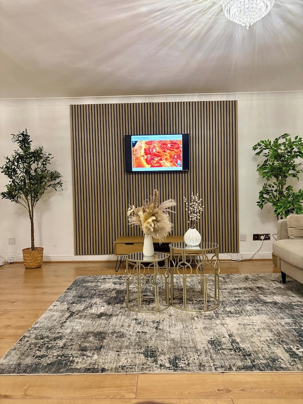 Un salon moderne avec un téléviseur à écran plat fixé au mur, une table basse ronde, un canapé et deux plantes en pot.