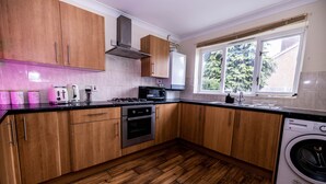 A modern kitchen with wooden cabinets, a built-in oven, a microwave, and a washing machine. - Sleeps8-kingbeds-sofabed-garden-aircon-freeparking (London)