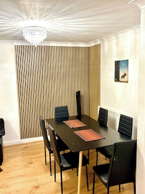 A dining area with a table, chairs, a chandelier, a wall-mounted picture, and a vertical slat wall. - Sleeps8-kingbeds-sofabed-garden-aircon-freeparking (London)