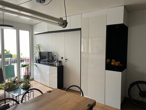 Cozy living space with a dining area, kitchen, and shelving unit.