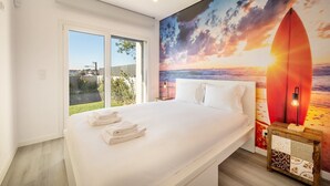 A bedroom with a large bed, a view of the outdoors, and a sunset mural on the wall. - GuestReady - Peaceful stay in Charneca da Caparica (Charneca de Caparica)