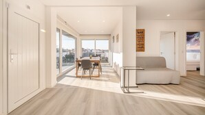 A modern interior with a dining area, a sofa, and a view through large windows. - GuestReady - Peaceful stay in Charneca da Caparica (Charneca de Caparica)