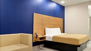 A hotel room with a bed, a bedside table with a phone, a chair, and a small table. - Scottish Inn Parker (Houston)