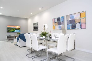 Un comedor moderno con una mesa de vidrio, sillas blancas y arte abstracto en las paredes.