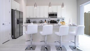 A modern kitchen with white cabinets, stainless steel appliances, and three white bar stools. - 5 min to Disney 2024 Unique 5 Suites Villa (Kissimmee)
