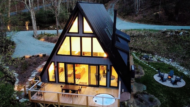 Une cabane moderne de forme triangulaire, dotée de grandes fenêtres, d’une terrasse en bois et d’un bain à remous.