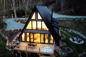 Una cabaña moderna de forma triangular con ventanas amplias, una terraza de madera y un jacuzzi.