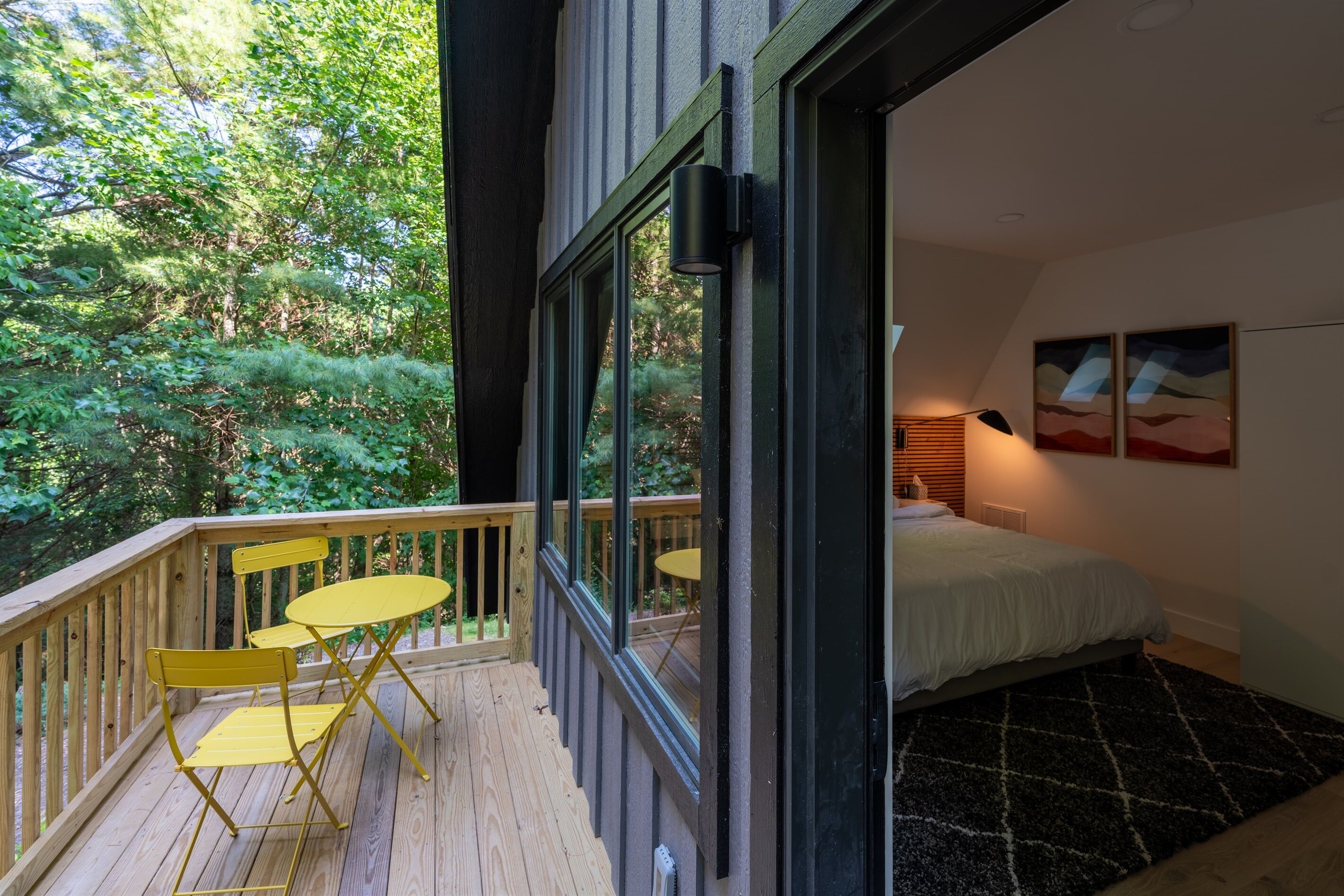 Une chambre avec une grande fenêtre, un lit et un petit balcon équipé d’une table et de chaises.