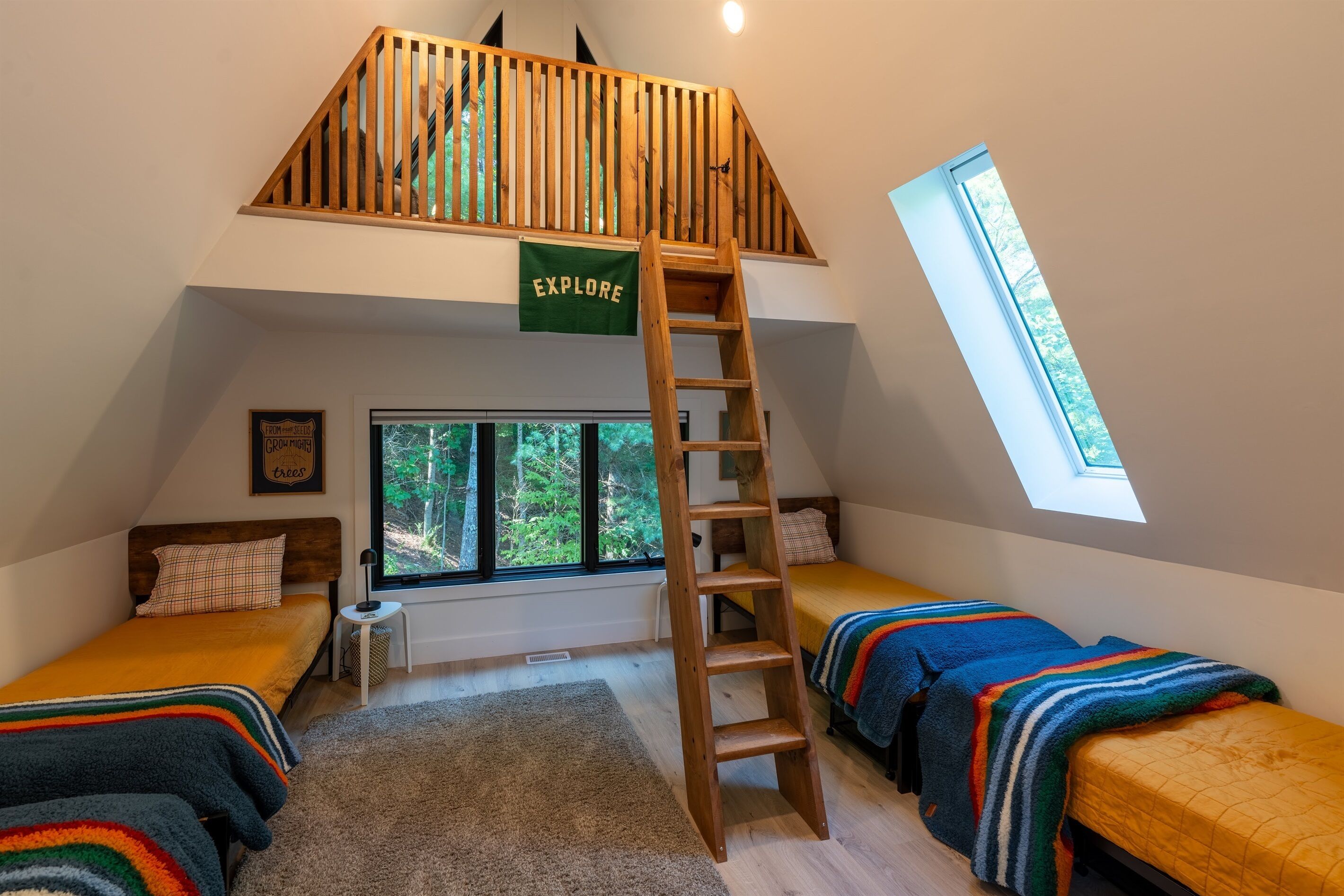 Ein Schlafzimmer im Loft-Stil mit einer Holzleiter, zwei Betten, einem Oberlicht und Blick auf Bäume.