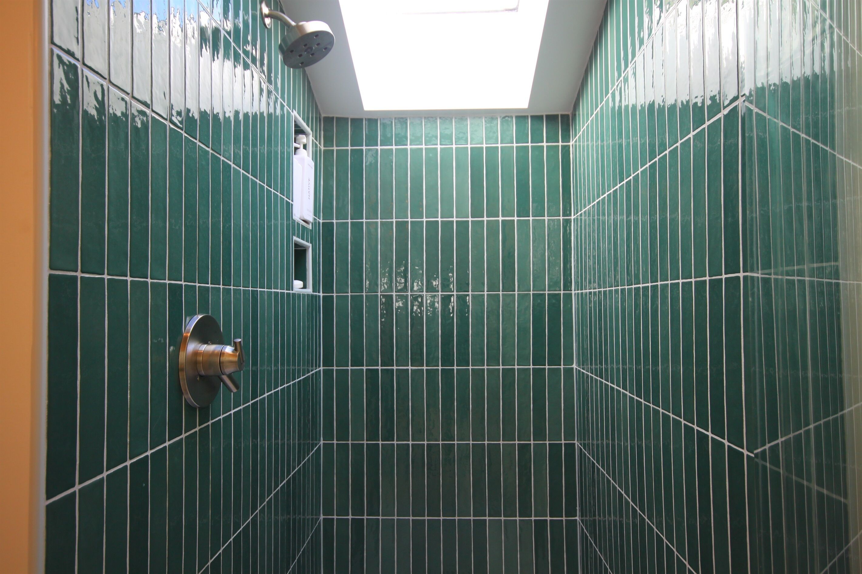 A bathroom with green tiles and a skylight.