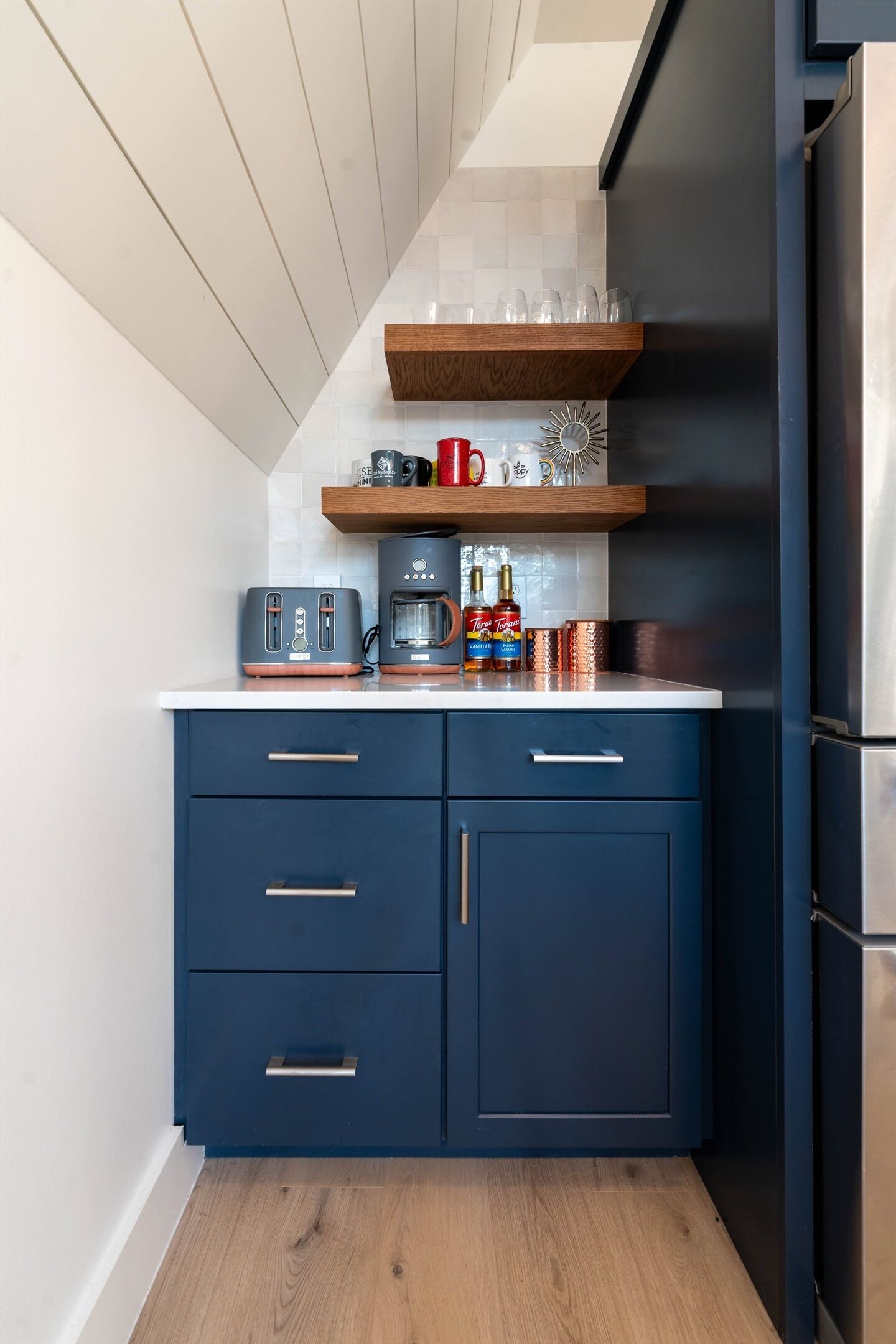 Una cocina compacta con armarios azul oscuro, encimera blanca y refrigerador de acero inoxidable.