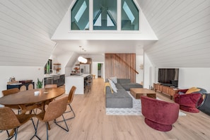A spacious living area with a high ceiling, a dining table, and a cozy seating arrangement.