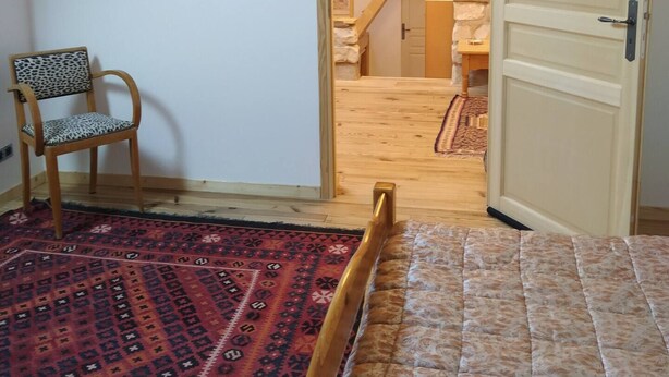 A bedroom with a bed, a chair, a patterned rug, and a wooden door leading to a staircase. - Charming and comfortable apartment in a very pleasant farmyard (Achères-la-Forêt)
