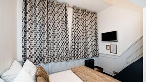 A bedroom with a bed, pillows, a fur throw, a TV on the wall, and a staircase.