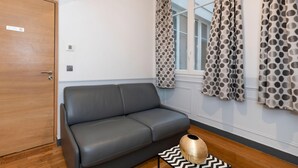 A room with a grey sofa, a wooden door, a window with polka dot curtains, and a small rug.