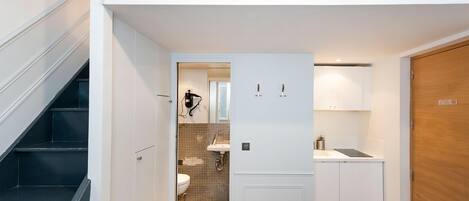 A compact, modern apartment with a loft bedroom, a kitchenette, and a bathroom with a tiled floor.