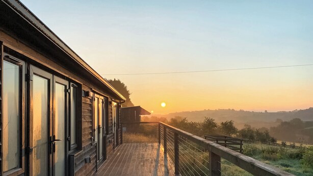 A wooden building with large windows and a balcony overlooking a rural landscape during sunset. - 2 bedroom accommodation in Presteigne (Presteigne)